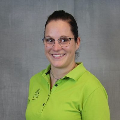 Porträt einer lächelnden Mitarbeiterin des Osteopathiezentrums in grünem Poloshirt vor hellem Hintergrund.