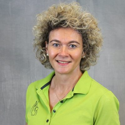 Porträt einer lächelnden Mitarbeiterin des Osteopathiezentrums in grünem Poloshirt vor hellem Hintergrund.