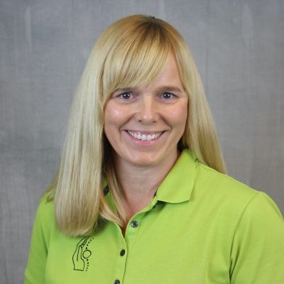 Porträt einer lächelnden Mitarbeiterin des Osteopathiezentrums in grünem Poloshirt vor hellem Hintergrund.