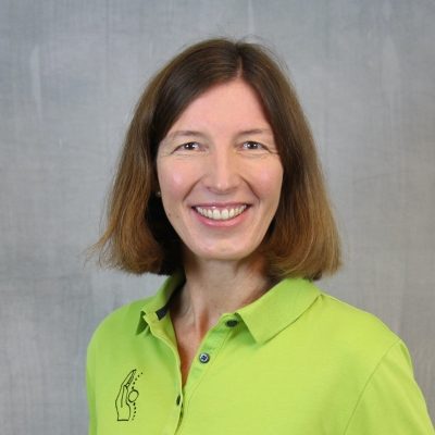 Porträt einer lächelnden Mitarbeiterin des Osteopathiezentrums in grünem Poloshirt vor hellem Hintergrund.