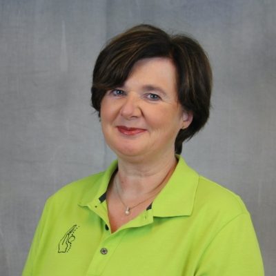 Porträt einer lächelnden Mitarbeiterin des Osteopathiezentrums in grünem Poloshirt vor hellem Hintergrund.